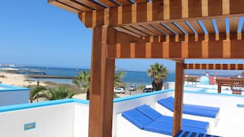 Uma pérgola de madeira com espreguiçadeiras azuis com vista para uma praia e oceano.