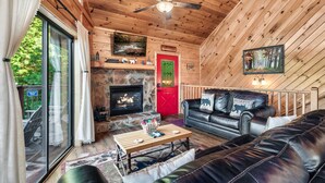 Een gezellig cabin interieur met een stenen open haard, een leren bank en een plafondventilator.