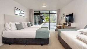 A hotel room with two beds, a TV, a desk, and a view through a glass door.