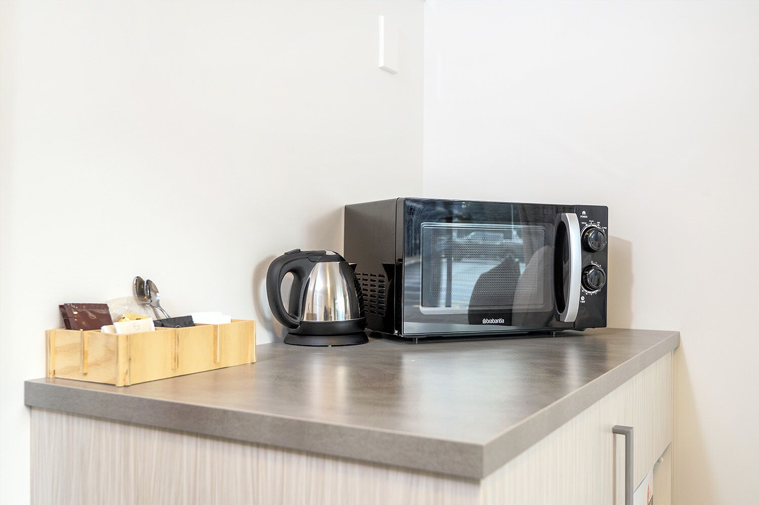 Un microondas y una tetera sobre una encimera de cocina con un organizador de madera que contiene utensilios.