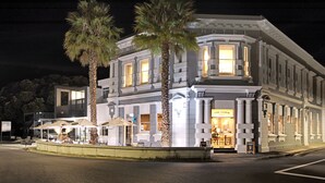 A hotel with a classic facade, palm trees, and outdoor seating. - The Com Plex Motel (Whakatane)