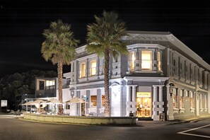 A hotel with a classic facade, palm trees, and outdoor seating.