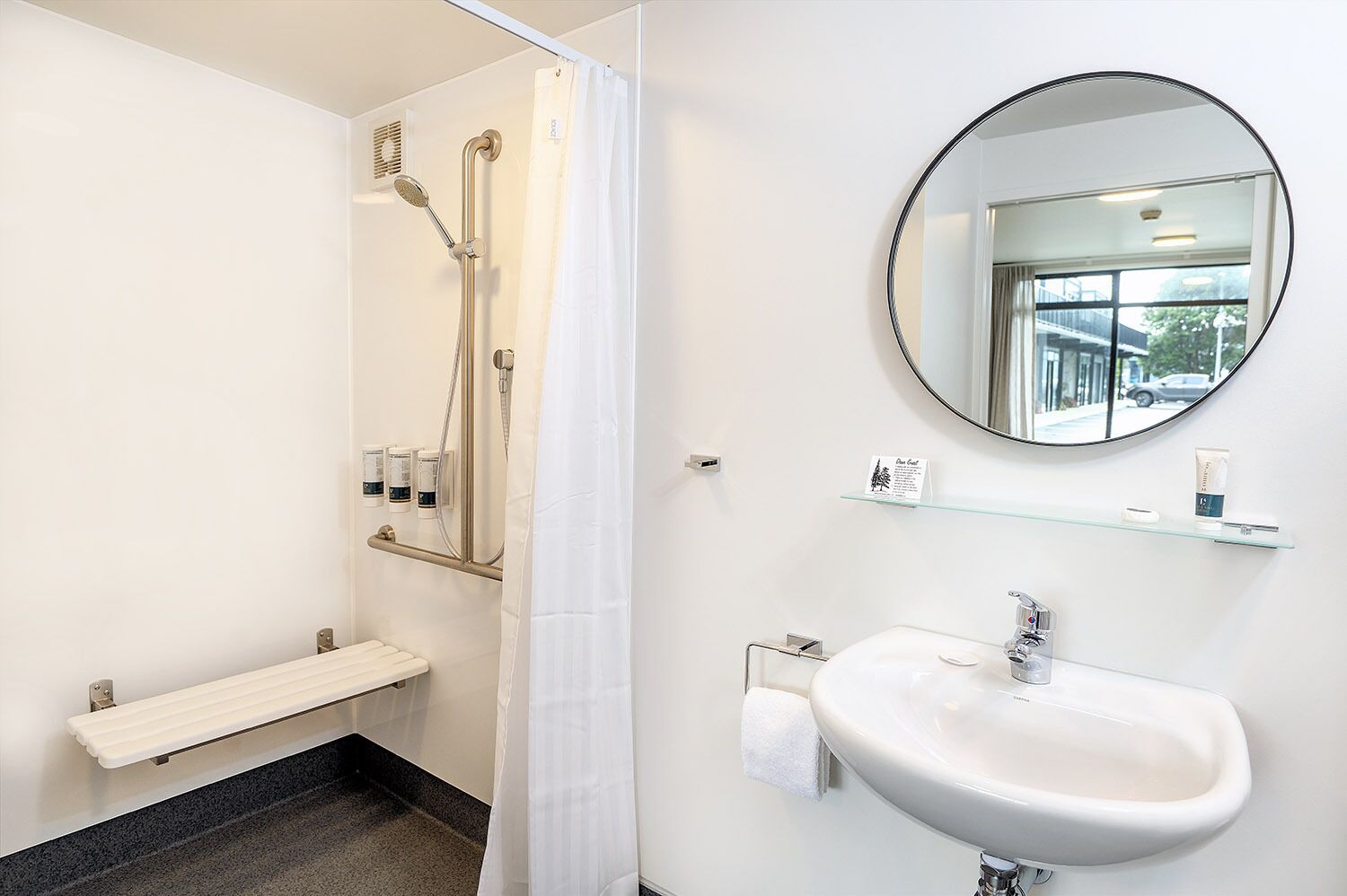 A modern bathroom with a shower, a sink, a mirror, and a shelf with toiletries.