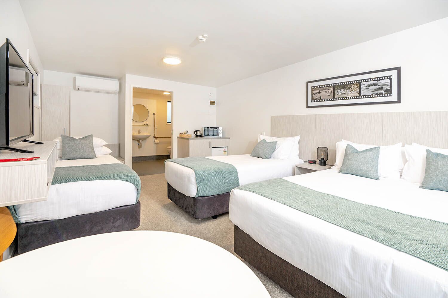 Een hotelkamer met twee bedden, een bureau met televisie, een badkamer en een lijst aan de muur.