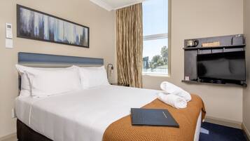 A hotel room with a bed, a painting on the wall, a television, and a window with curtains.