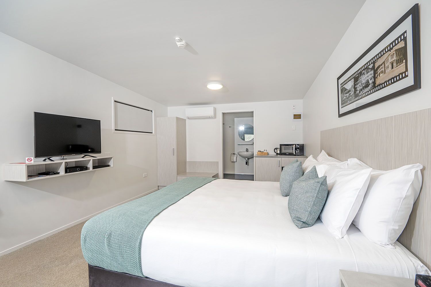 Ein modernes Hotelzimmer mit einem großen Bett, einem Flachbildfernseher, einer Mikrowelle und einer kleinen Küchenzeile.