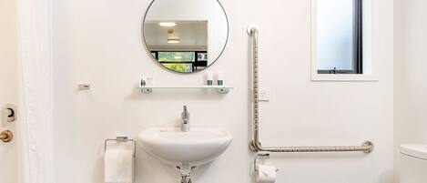 A bathroom with a round mirror, a sink, a toilet, and a window.