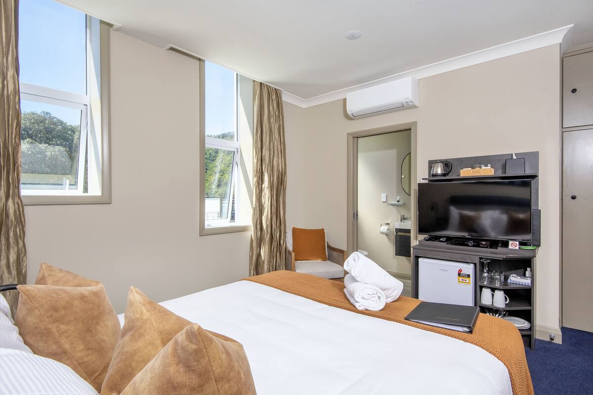 Habitación de hotel con cama, televisor, refrigerador pequeño y escritorio con computadora portátil.