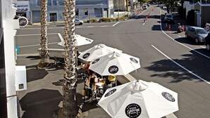 Outdoor seating with umbrellas, palm trees, and a street view with cars and buildings.