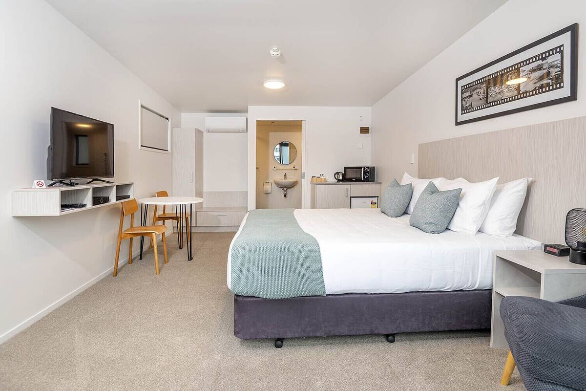 Una habitación de hotel moderna con una cama, un escritorio, una silla, un televisor y un microondas.