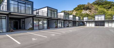 A modern hotel with a row of rooms, a parking lot, and a natural backdrop.