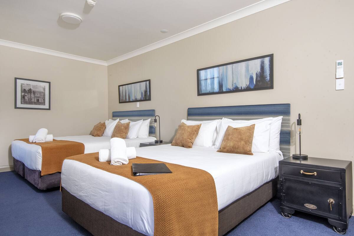 Habitación de hotel con dos camas, una mesita de noche y una lámpara de pared.
