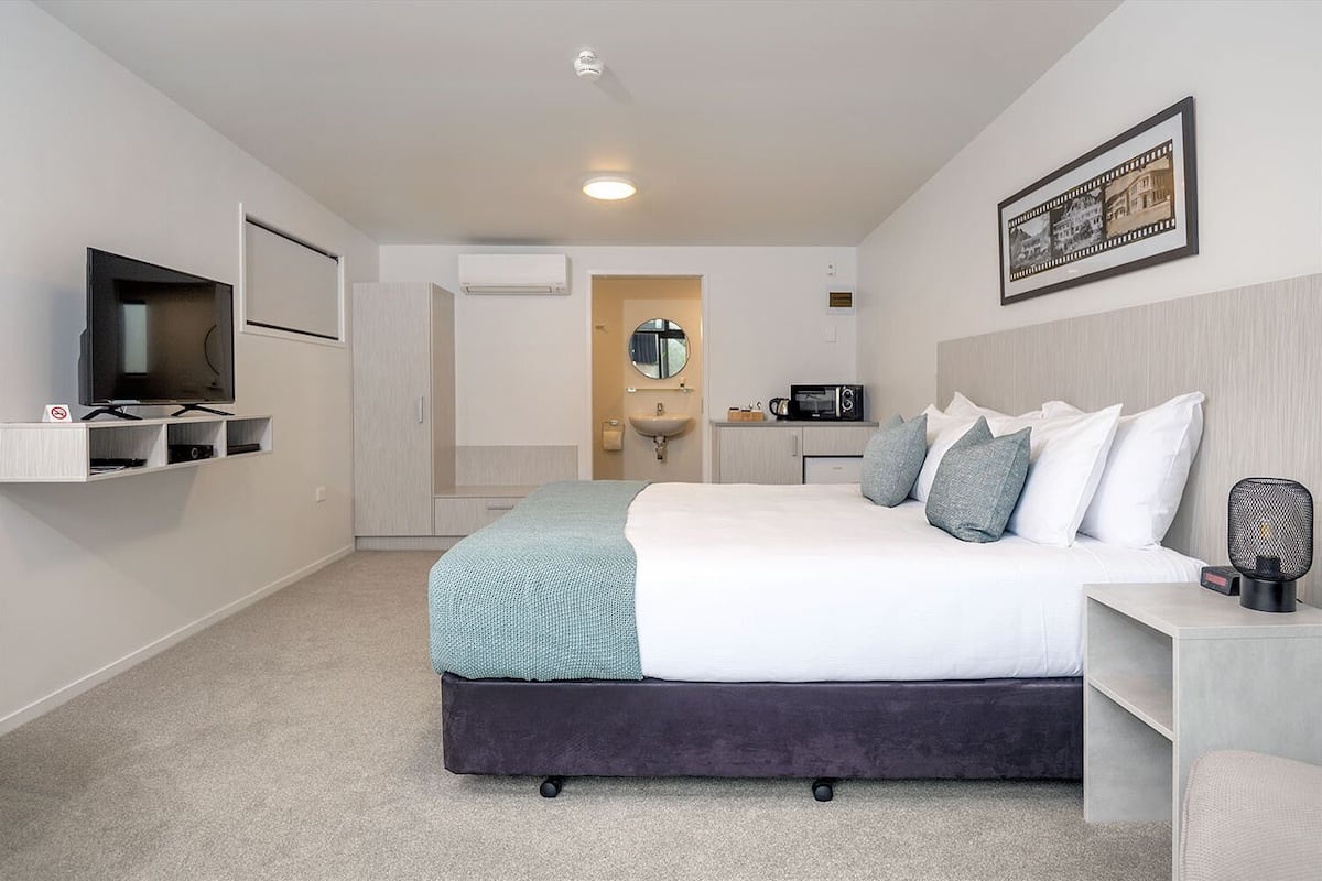 Una habitación de hotel moderna con una cama grande, televisión, microondas y lavamanos.