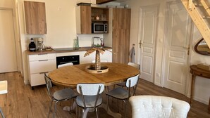 Una cucina compatta con mobili in legno, un forno a microonde e una macchina da caffè. C'è un tavolo da pranzo con quattro sedie e un centrotavola con una pianta decorativa.