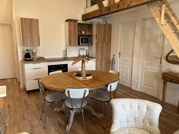 A compact kitchen with wooden cabinets, a microwave, and a coffee maker. There is a dining table with four chairs and a decorative plant centerpiece. - Lapolline (Wimereux)