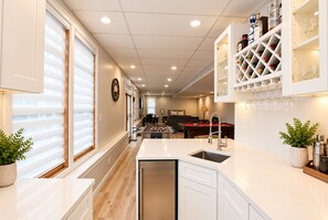 A modern kitchen with a central island, a dining area with a pool table, and a bar area with wine bottles and glasses.