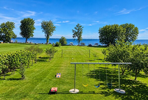 A well-maintained grassy area with a swing set, a small shed, and a view of the sea.