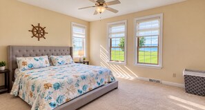 A bedroom with a large bed, a ceiling fan, and windows with a view of a golf course.