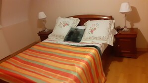 Una cama bien hecha con un edredón a rayas, dos mesitas de noche con lámparas y almohadas estampadas con motivos florales.