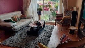 Una sala de estar con un sofá, una mesa de centro, un televisor, una silla y vistas a un balcón con flores.