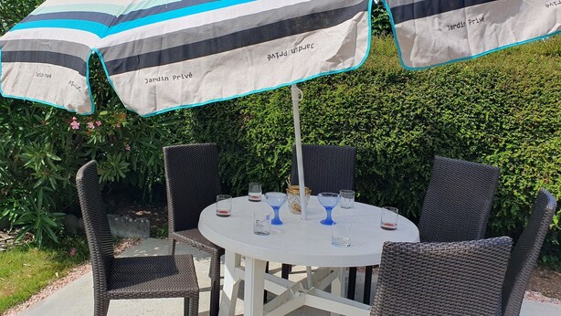 Una mesa redonda con sillas de mimbre y sombrillas a rayas, con la etiqueta 'Jardin Privé'.