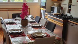 Un comedor con una mesa dispuesta para cuatro personas, un florero con flores rosas y una cocina con estufa y microondas.