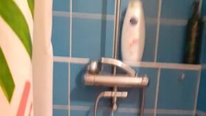 Un baño con paredes de azulejos azules, una ducha con cabezal de ducha manual y una cortina blanca con estampado floral.