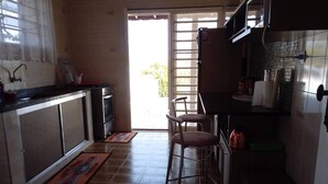 Una cocina con piso de baldosas, un lavamanos, una estufa y un refrigerador. Hay una puerta que da al exterior.