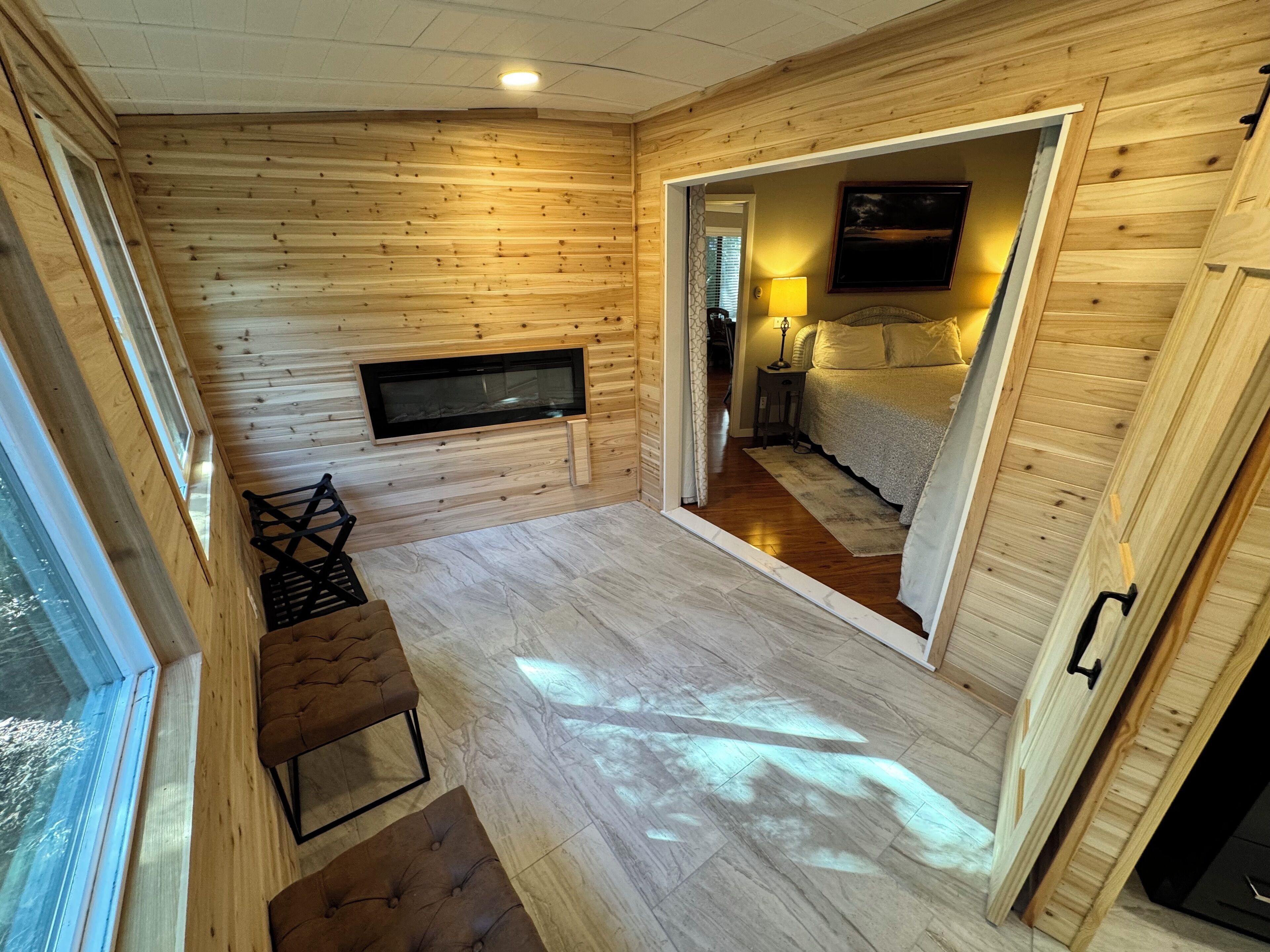 A wooden interior with a TV mounted on the wall, a sofa, and a bed in the adjacent room.
