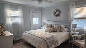 Een slaapkamer met een bed, nachtkastje, stoel, plafondventilator, deur en raam met jaloezieën.