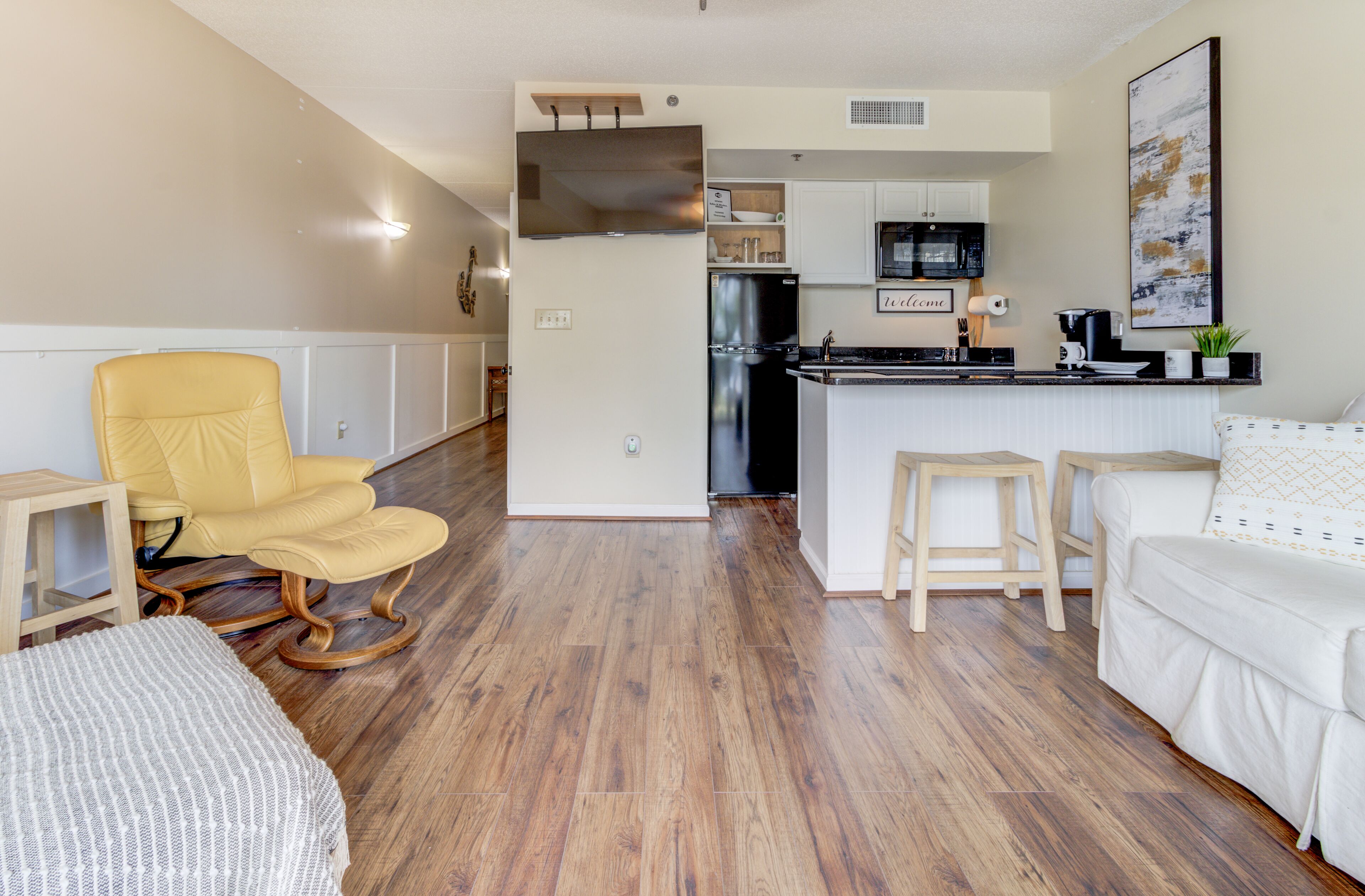 A modern kitchen with a central island, wooden flooring, and a yellow rocking chair.