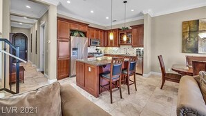 A spacious kitchen with wooden cabinets, a central island with bar stools, and a dining area with a table and chairs. - Condo at  Prestigious gated V community (Henderson)