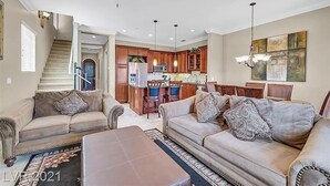 A spacious living room with two sofas and a coffee table, a kitchen with wooden cabinets, and a dining area with a chandelier. - Condo at  Prestigious gated V community (Henderson)