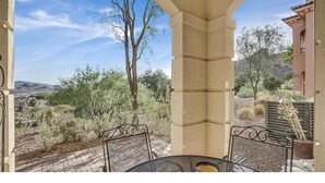 A patio with a table and chairs, overlooking a desert landscape with trees and distant hills. - Condo at  Prestigious gated V community (Henderson)