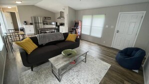 Een moderne woonkamer met een bank, salontafel en een relaxfauteuil. In de achtergrond is een keuken te zien.