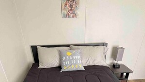 Een bed met een donkere matras en twee kussens, waarvan één een vrolijke boodschap heeft.