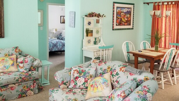 Una habitació amb sofàs de motius florals, una taula de dinar amb cadires i un ventilador de sostre.