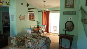 Un saló amb un sofà, una taula de dinar amb cadires, una làmpada penjant i un rètol que diu 'BEACH HOUSE'.