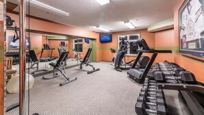 A gym with cardio machines, weight benches, and dumbbells.