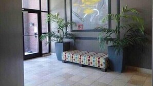 Eine Lobby mit Fliesenboden, einer Bank, Topfpflanzen und einem großen, abstrakten Gemälde an der Wand.