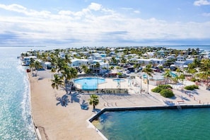 Relax by the central pool surrounded by palm trees and umbrellas, with access to the sandy beach and ocean views.