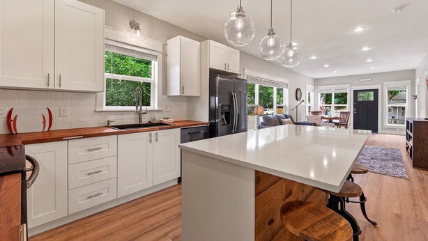 Une cuisine moderne avec des meubles blancs, un grand îlot central et des luminaires suspendus.