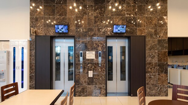 A modern elevator area with marble walls, two elevators, and a digital display above each. - Toyoko Inn Tokyo Akishima-eki Minami-guchi (Akishima)
