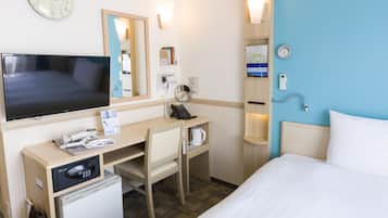 Una habitació d'hotel amb un llit, un escriptori amb un ordinador, un frigorífic, un microones, un rellotge, un mirall i un telèfon fixat a la paret.
