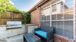 An outdoor patio with a grill, wicker furniture, and a brick wall.