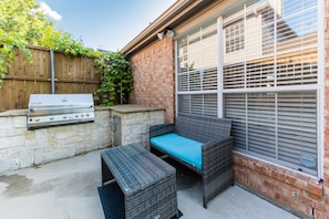 An outdoor patio with a grill, wicker furniture, and a brick wall.