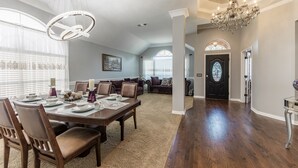A spacious dining area with a large wooden table, multiple chairs, and a chandelier.
