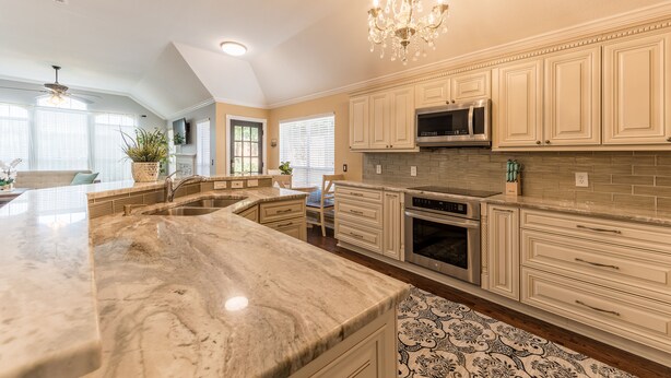 A spacious kitchen with marble countertops, a built-in microwave, and a chandelier.