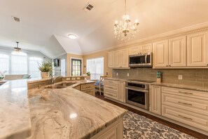 A spacious kitchen with marble countertops, a built-in microwave, and a chandelier.