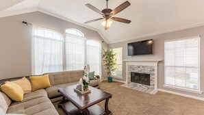 A living room with a sectional sofa, a coffee table, a fireplace, and a ceiling fan.
